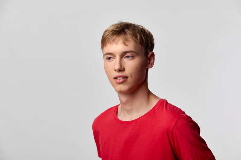 Red shirt, casual male in a studio setting with clean lighting, relaxed pose and plain background, highlighting contemporary fashion and everyday wardrobe for modern lifestyle visuals