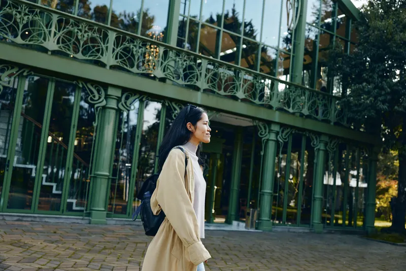 woman, coat, backpack, outdoor, architecture, walkway, urban, fashion, strolling along a glass facade, daylight, calm street scene, travel vibe, discovering new surroundings