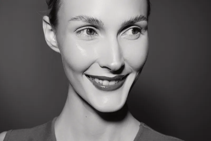 Smiling Caucasian woman with pale skin looks aside in black and white portrait. Soft lighting highlights facial features and natural expression.