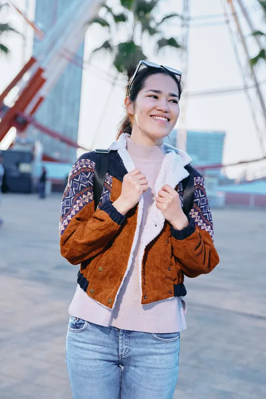 jacket outdoor smile fashion casual street urban daylight a cheerful woman wears a brown patchwork jacket and jeans with sunglasses on her head posing in a bright city street for a candid street