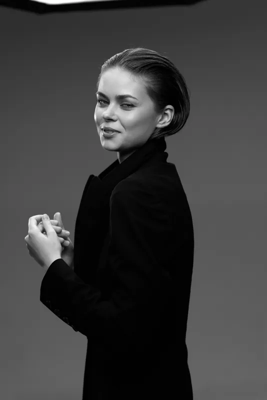Black and white portrait of smiling woman in elegant dark jacket with short hair and confident expression.
