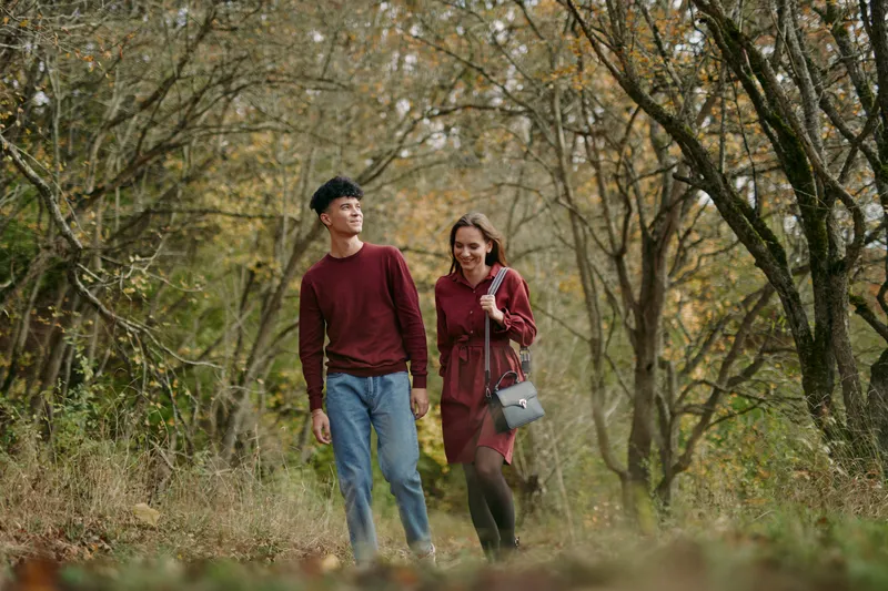 A young couple walking through an autumn forest, captured in a candid and authentic moment that conveys credibility and genuine connection during a relaxed outdoor stroll among trees.