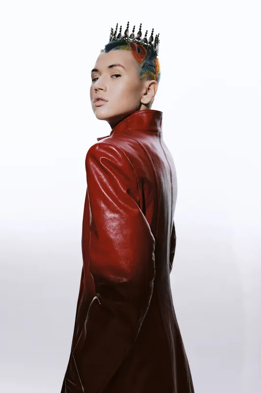 rebellious woman with crown wearing red leather coat stands confidently against white background, showcasing unique style and bold fashion statement in studio setting
