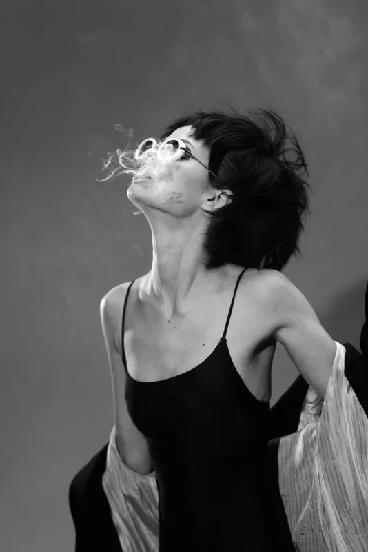 black and white artistic portrait of smoking woman with glasses, dark hair, and elegant style expressing attitude in studio