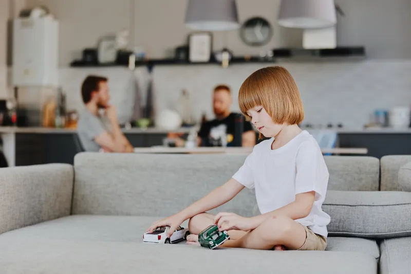 Young boy playing with toy cars in a stylish living room, showcasing creativity and childhood joy in a modern family setting.