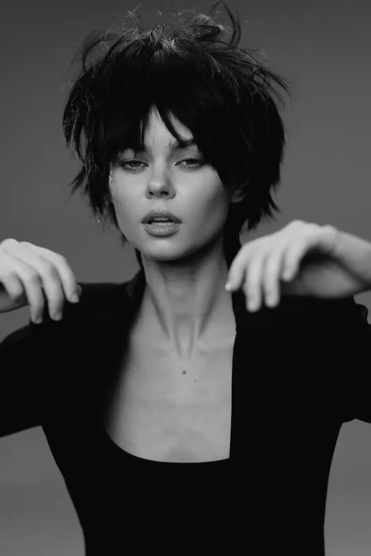 Black and white portrait of a young woman with short messy hair and serious expression wearing dark clothing