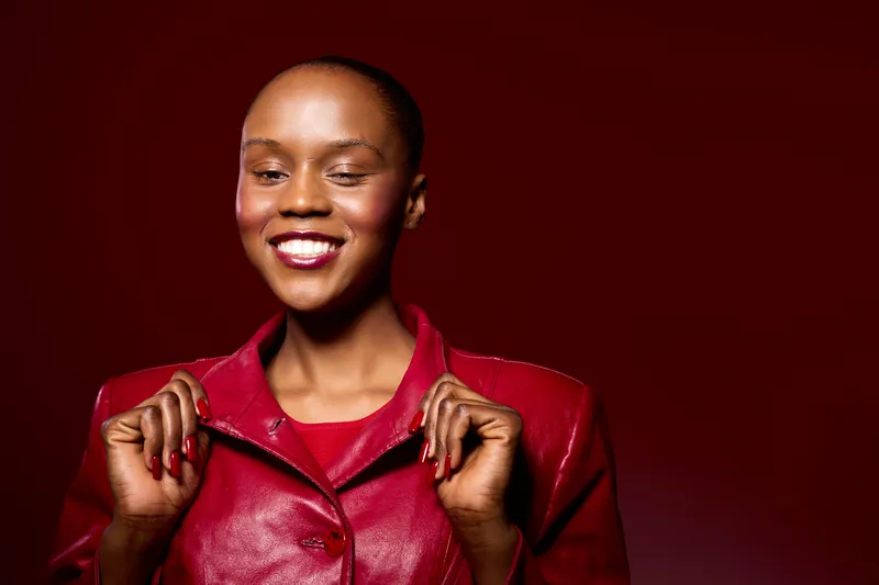 Confident smiling black woman with dark skin wearing red leather jacket on red background. Portrait of happy African female model showing positive emotions and stylish fashion look.