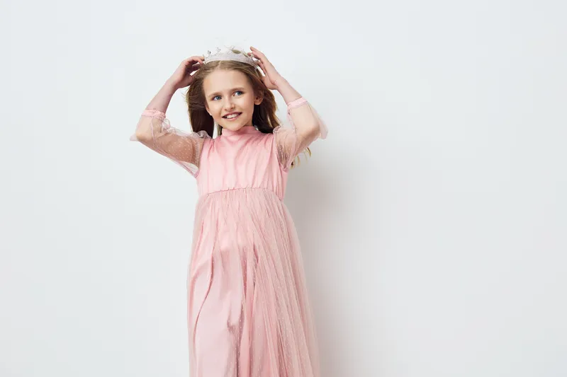 A joyful girl wearing a pink dress and a flower crown, celebrating joy and innocence in a bright, minimalist setting Perfect for seasonal events