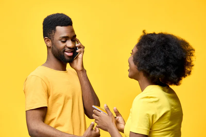 Happy African couple talking on the phone against a vibrant yellow background, wearing matching yellow outfits, expressing joy and connection