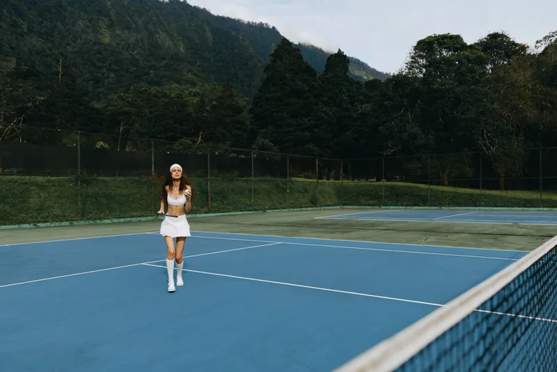 Smiling young female athlete playing tennis on a blue court surrounded by lush greenery, showcasing a dynamic and energetic sports lifestyle