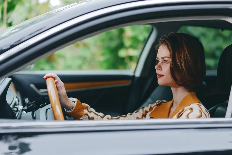 A smiling woman driver sits comfortably in the car seat, hand on the steering wheel, ready for a journey and confident behind the wheel.