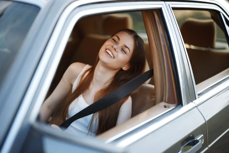 Young woman enjoying a sunny day in a car, smiling and relaxed, with her hair flowing in the breeze, conveying a sense of freedom and adventure.
