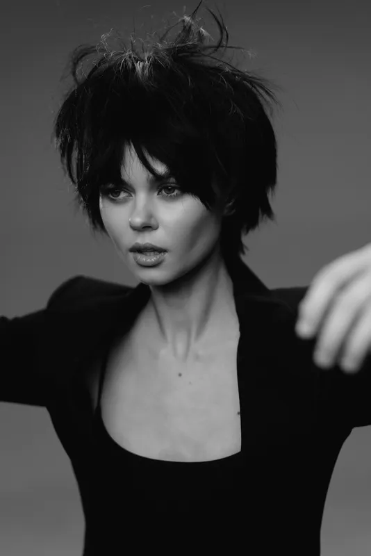 Black and white portrait of a young woman with short dark hair wearing a black top, expressing intensity and focus.