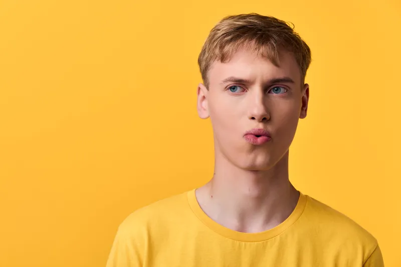Closeup of a man in a yellow shirt making a pouty expression against a bright backdrop, studio lighting highlighting color and mood, casual fashion vibe for lifestyle and social media shots.