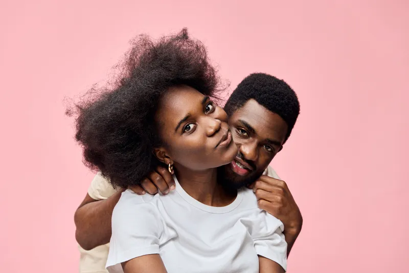 Young African couple sharing a playful moment against a soft pink background, showcasing joy and connection, perfect for themes of love and companionship