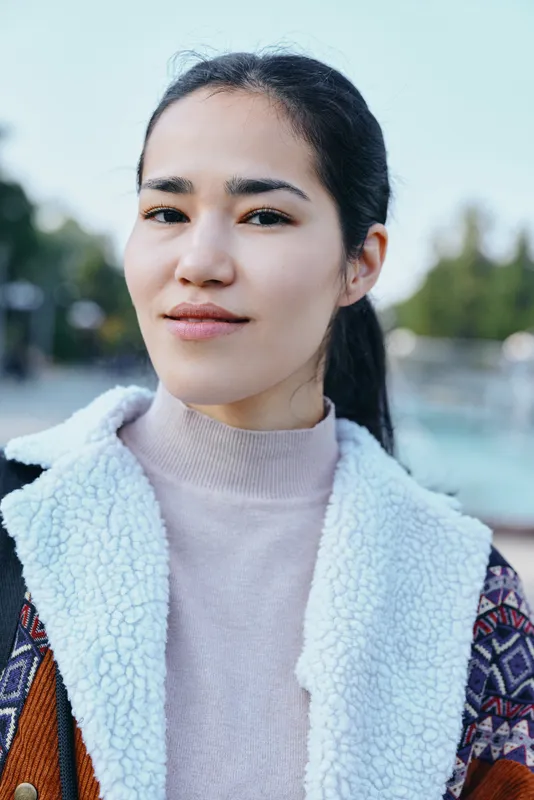 Woman wearing a soft fleece coat and layered knit standing outdoors with soft sunlight and blurred trees conveying casual style, comfort, and urban freshness for fashion and lifestyle imagery
