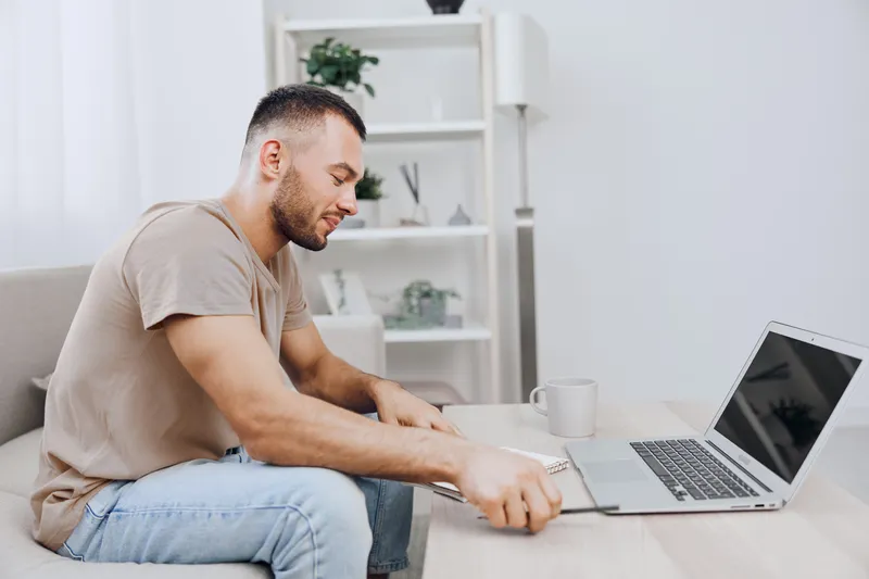 Focused man working on a laptop at home, showcasing a modern workspace with minimalistic decor and natural light. Perfect for remote work themes in 2025.