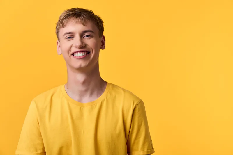 Smiling man against a bright yellow background wearing a yellow shirt, exuding warm cheerful energy in a simple studio shot with soft lighting and casual vibe