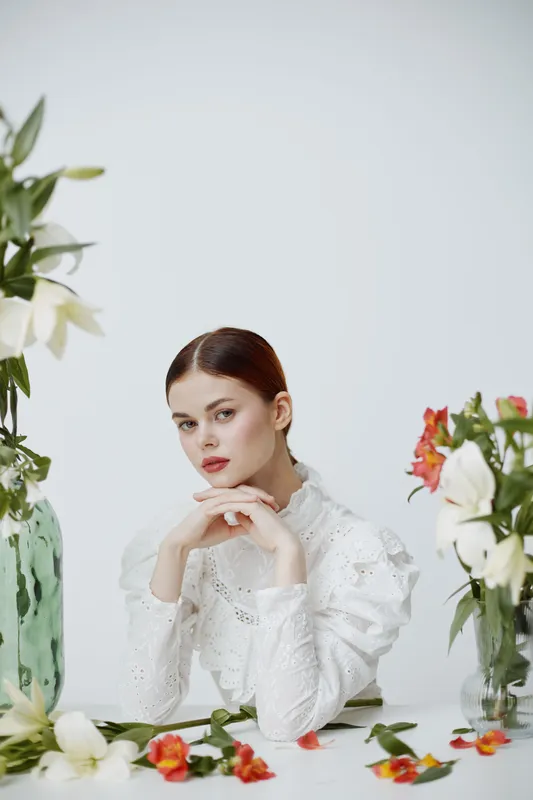 Elegant young woman in white blouse with flowers, showcasing beauty, serenity, and femininity against a soft, neutral background