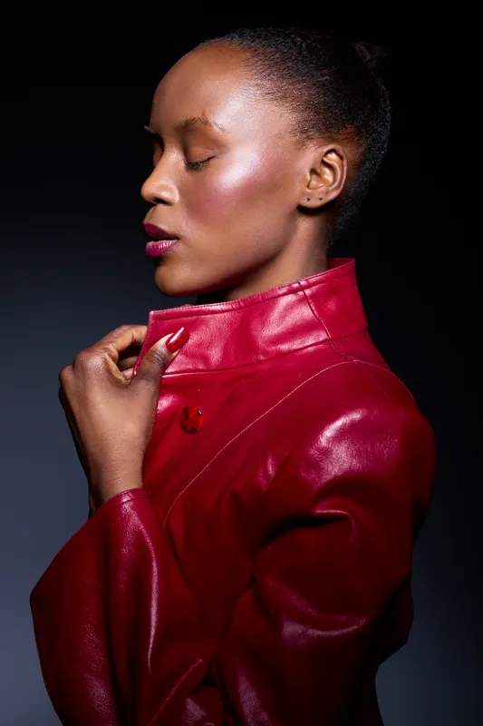 Profile of a black African woman with dark skin and closed eyes wearing a red leather jacket. Studio portrait with dramatic lighting on black background, concept of fashion and elegance.