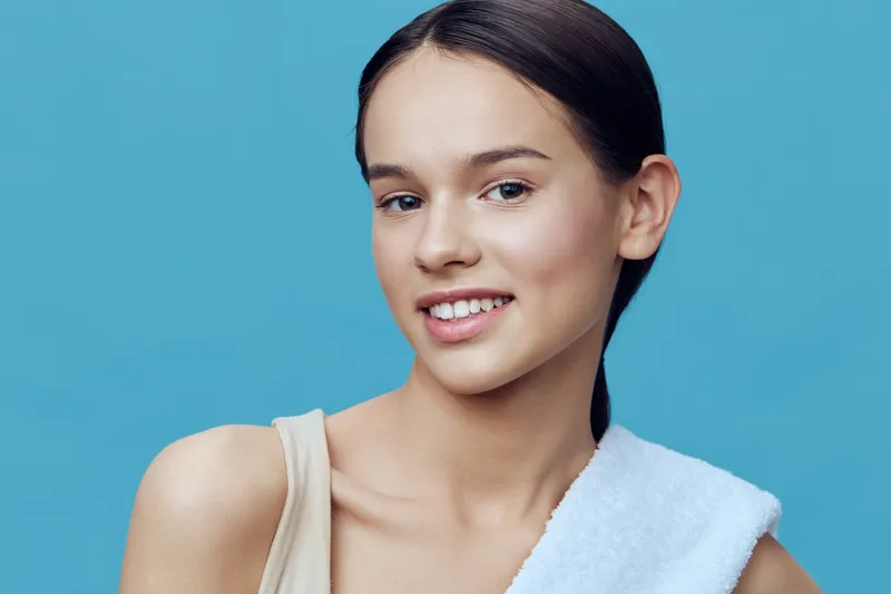 Young woman with a towel displaying a confident smile against a vibrant blue background, embodying self care and wellness in a fresh and modern lifestyle