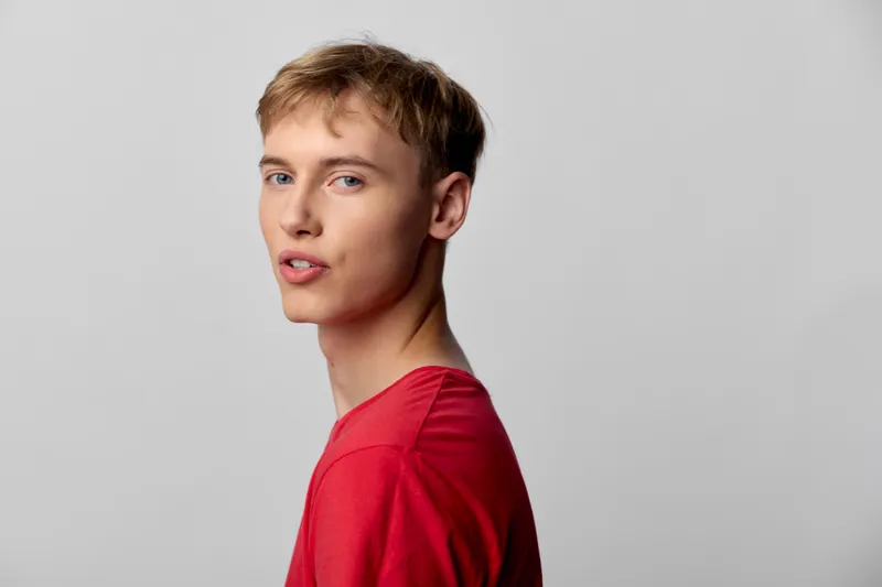 Young man in a red shirt shown in studio lighting with a side profile, casual expression, clean background, contemporary headshot vibe for fashion and lifestyle use