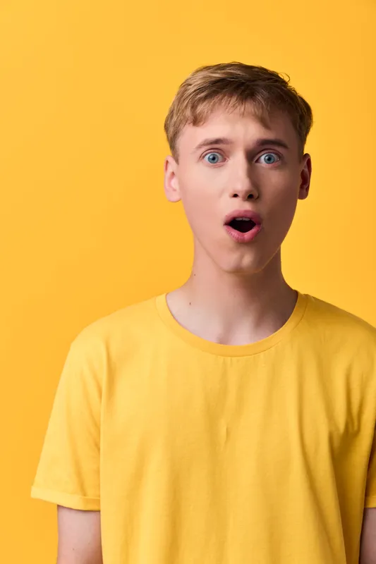 Surprised man in a yellow shirt against a bright yellow background, a wide-eyed open-mouthed expression conveys curiosity and astonishment in a studio setting