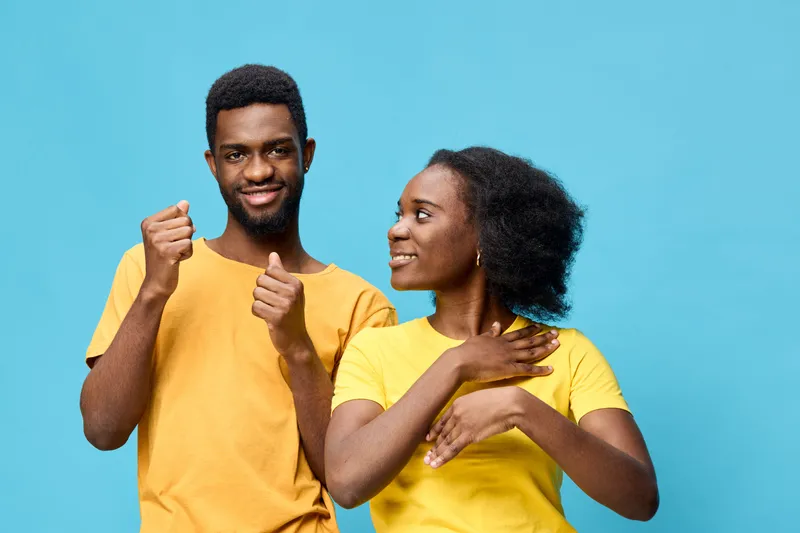 Two young Black adults expressing joy and connection with thumbs up and a smile against a bright blue backdrop, conveying happiness and friendship