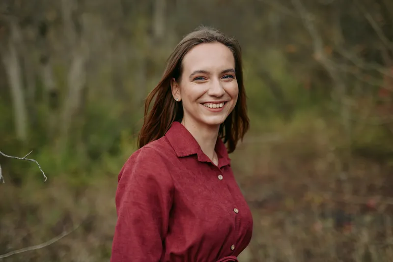 Candid outdoor portrait of a smiling young woman in a red shirt, natural expression, soft lighting and relaxed posture conveying authenticity and trustworthiness for genuine lifestyle imagery.