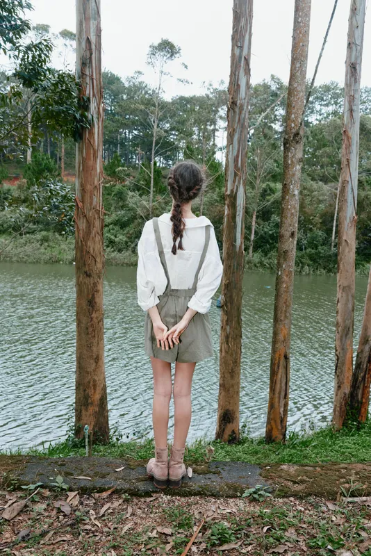 Young woman standing by the serene lake, wearing a white blouse and a casual skirt, surrounded by nature on a calm day