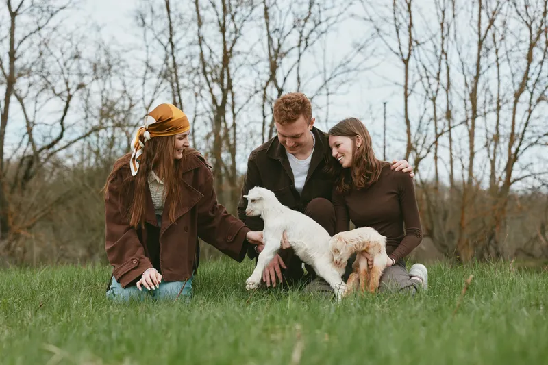 Family, outdoor, dogs, friends enjoying a sunny park scene, a candid moment of bonding and affection, warm clothing and green grass, natural light, casual lifestyle in a rural setting