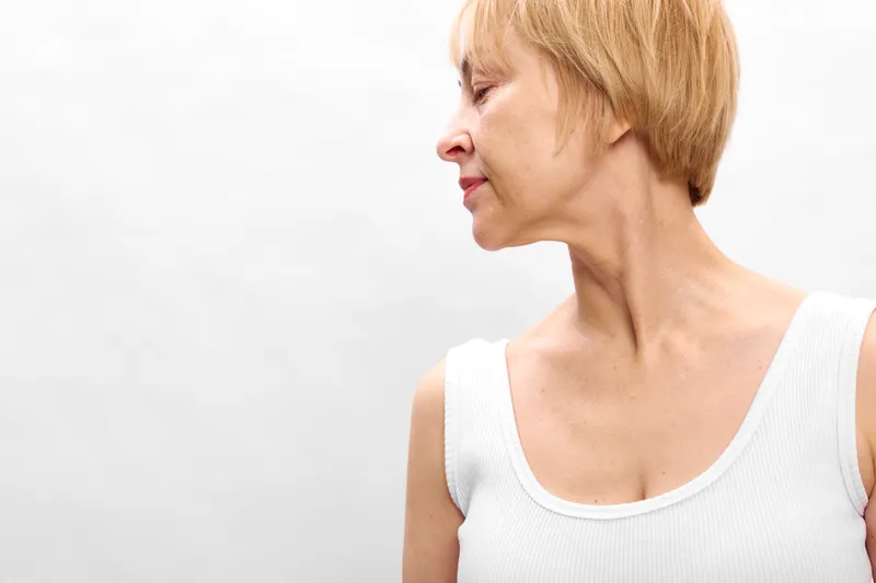 Woman profile with short blonde hair, calm expression, side view portrait, wearing white sleeveless top. Clean white background and soft light create peaceful mood