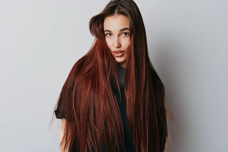 Woman with long straight hair and natural makeup posing against white background. Young female model with red hair wearing black t shirt looking at camera with soft expression.