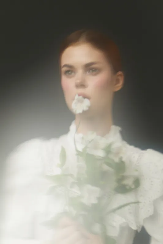 Young woman holding white flowers with a soft focus, wearing a vintage blouse, conveying tranquility and natural beauty in a dreamy atmosphere