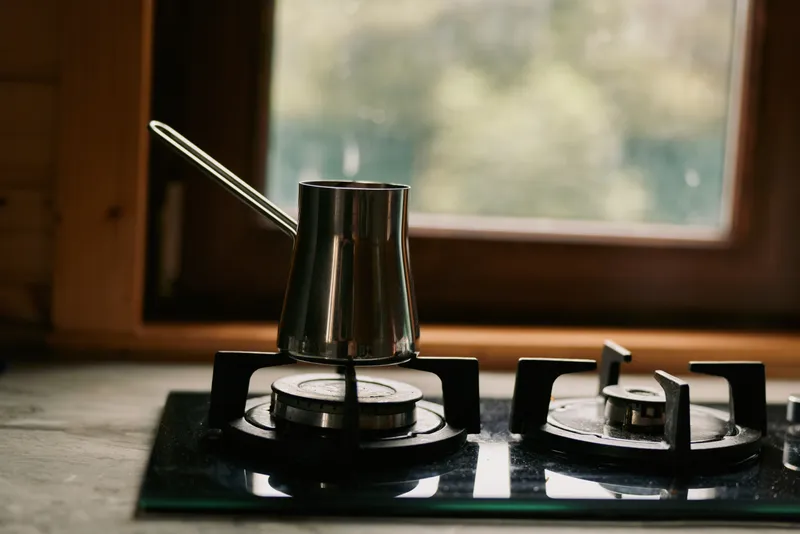 Stove with kettle on gas burner in kitchen, a metal pot and rising flame, capturing a moment of cooking and warm heat in a simple domestic scene. The light adds warmth and mood.