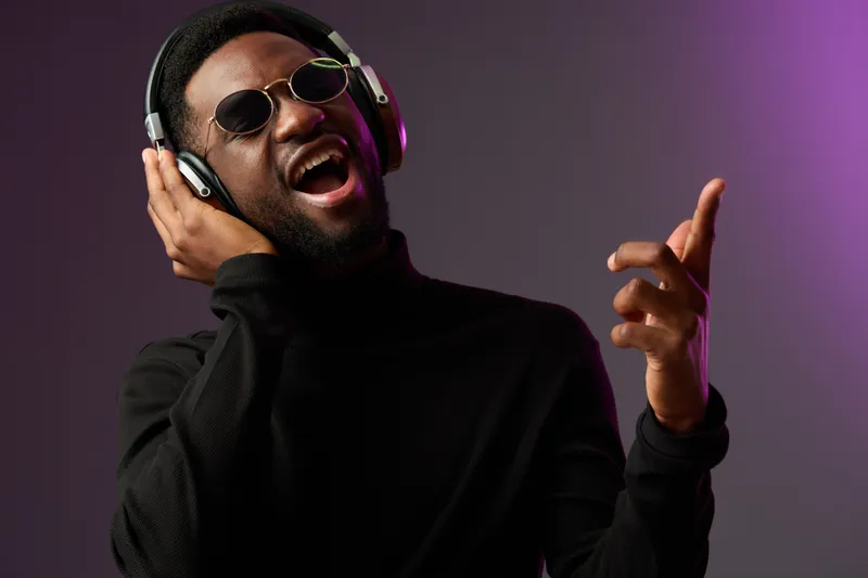 Young Black man wearing headphones and sunglasses, enjoying music passionately against a colorful gradient background