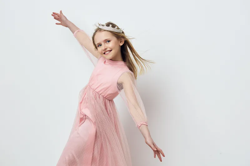 Happy young girl in elegant pink dress, celebrating childhood joy with playful expression, bright background, perfect for family and fashion concepts