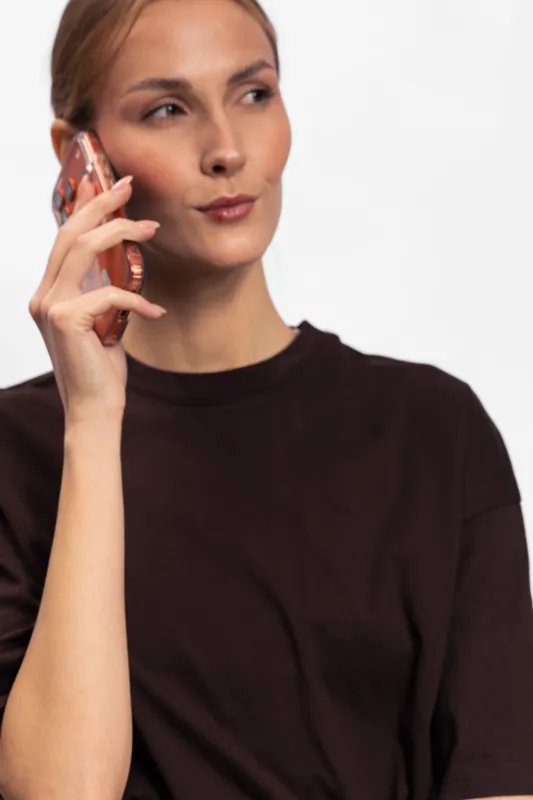 Young woman in black shirt holds smartphone near ear, looking to side with thoughtful expression. Modern communication and technology concept with white background and casual style.