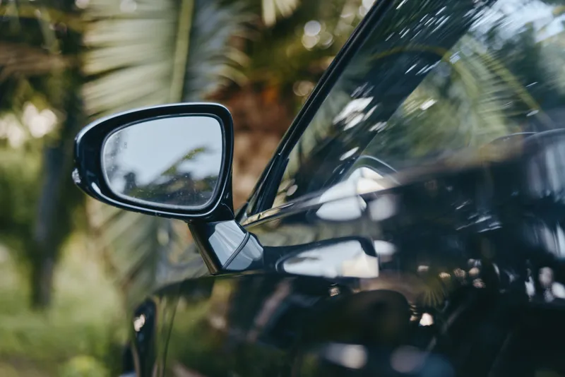 car side mirror black car palm trees reflection tropical closeup outdoor: glossy modern black luxury coupe mirror detail with palm reflections, sunlit bokeh, travel lifestyle vibe on roadside