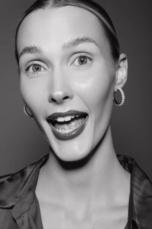 Close-up portrait of a smiling Caucasian woman with light skin and slicked-back hair in black and white. Concept for beauty, emotion, and natural expression.