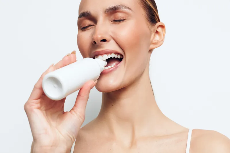 Young woman with closed eyes holds white bottle near mouth smiling natural skincare concept isolated on white background beauty routine and healthy lifestyle