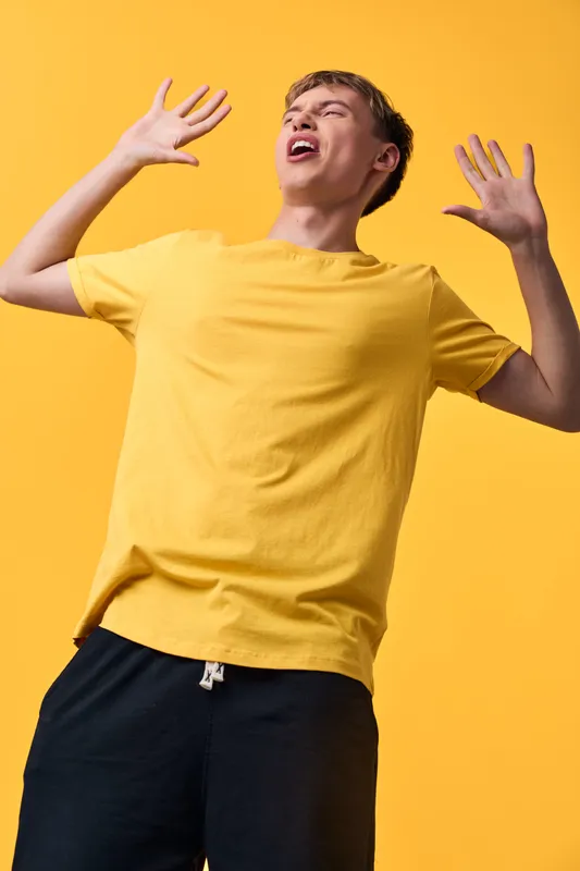 Youthful man in a yellow t shirt celebrates with open arms, energetic pose and bright studio backdrop, conveying joyful energy, casual style, and dynamic movement for fashion and lifestyle use