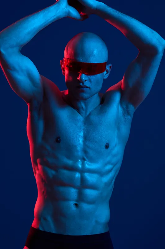 Athletic man showcasing a strong physique under dramatic lighting, with blue and red tones creating an energetic atmosphere. A visual representation of strength and vitality.