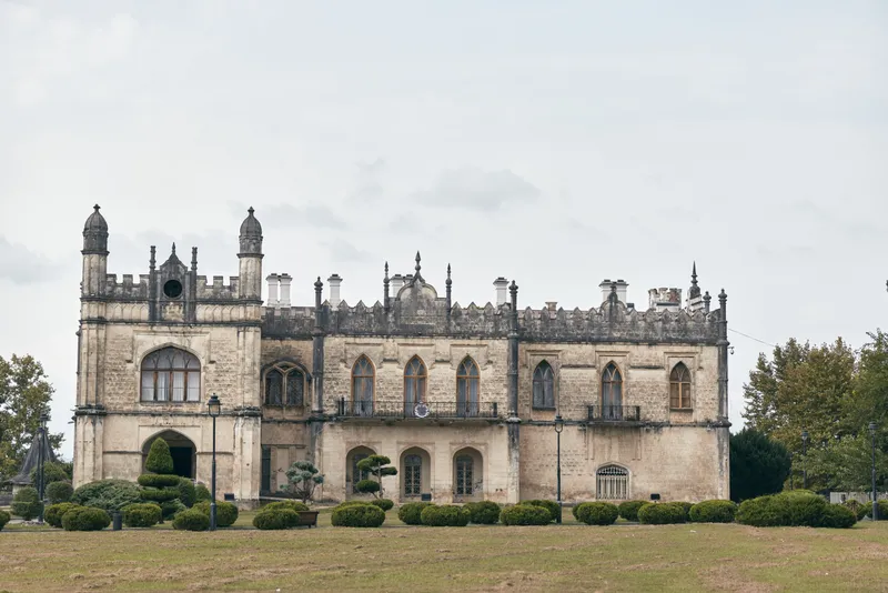 Castle ruins in a wide lawn setting, a historic stone building with arched windows and ornate battlements, creating a dramatic timeless landscape.