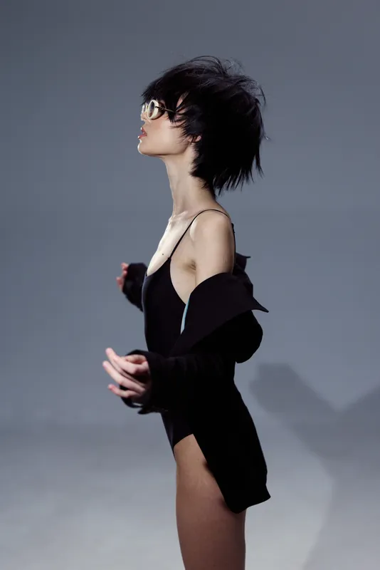 Profile of slim woman with short hair wearing glasses and black clothing against grey background.