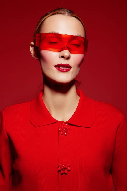 Portrait of a woman wearing red sunglasses and a red sweater against a red background. Fashion concept with bold colors and modern style, emphasizing monochrome and confident attitude.