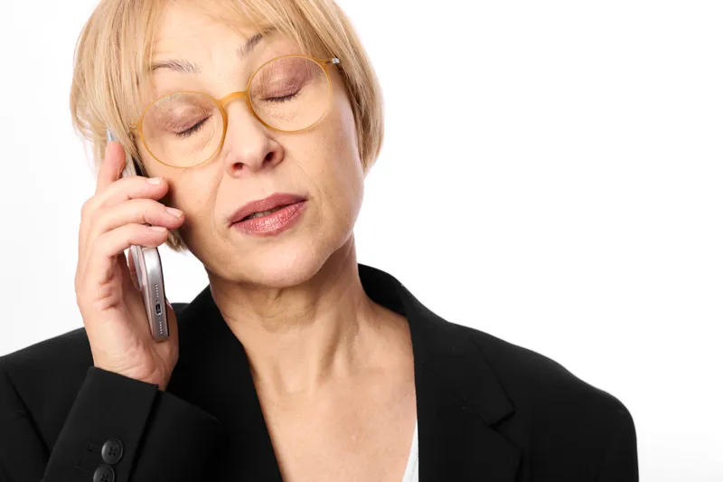 Woman elderly phone smartphone glasses business communication call portrait studio, she holds smartphone to her ear, serious tired expression, indoor close portrait on white background