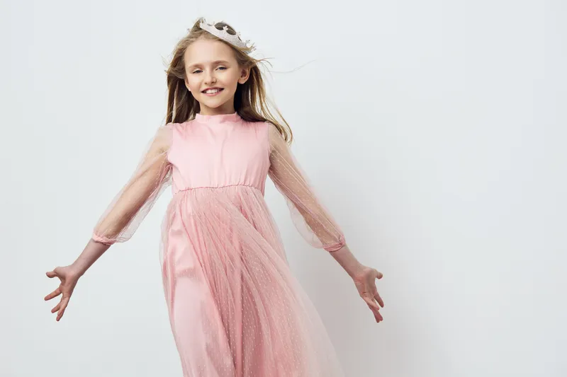 Cheerful young girl in a pink dress smiling joyfully, with flowing hair, against a soft pastel background, capturing the essence of childhood innocence and happiness