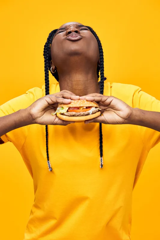 Happy girl enjoying a burger against a vibrant yellow background, showcasing joy and excitement for delicious food