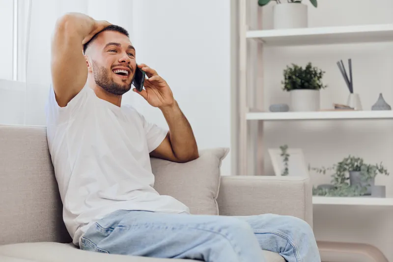 Happy man talking on the phone, experiencing moments of emotional connection and relaxation at home while enjoying a digital detox from technology.